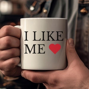 white coffee mug held by man with words i like me and a heart from the movie deadpool and wolverine