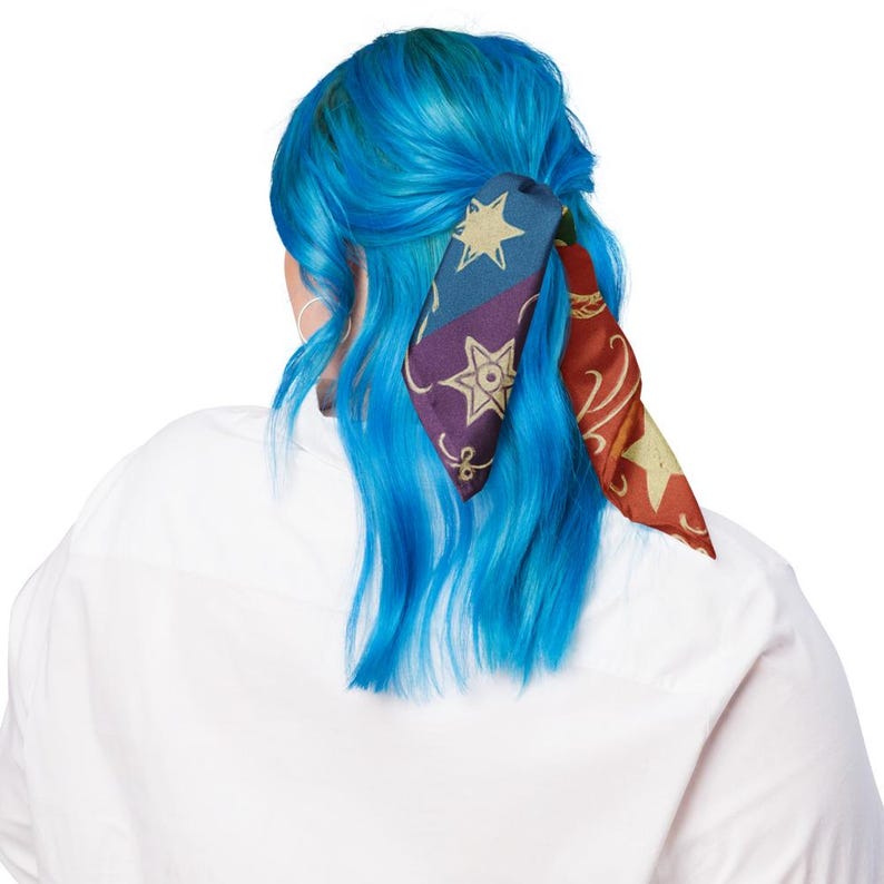 May include: A colorful silk scarf with star and geometric designs is tied in the hair. The scarf features a navy blue, purple, and red color scheme with gold star accents. The person is wearing a white shirt.