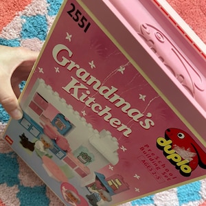 Op de afbeelding: Roze Duplo voorschoolse bouwset doos, getiteld "Grandma's Kitchen". De doos toont een keuken scène illustratie met witte, roze en blauwe elementen. Het Duplo logo is zichtbaar, samen met de leeftijdscategorie 2-5.