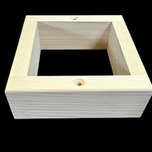 Könnte beinhalten: Ein helles, unfertiges Holzrahmen mit quadratischer Form. Der Rahmen hat eine hohle Mitte und besteht aus mehreren Holzstücken, die miteinander verbunden sind. Kleine Löcher sind in die obere Oberfläche gebohrt.