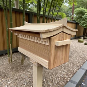 以下が含まれることがあります： 日本の建築デザインの木製郵便ポスト。明るい色の木材で作られており、傾斜した屋根、装飾的なトリム、ハンドルが付いています。木製の柱に取り付けられ、庭に設置されています。