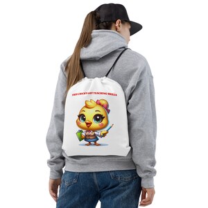 May include: White drawstring bag with a cartoon image of a yellow chick wearing glasses and holding a pencil. The text "This chick's got teaching skills" is printed in red on the bag.