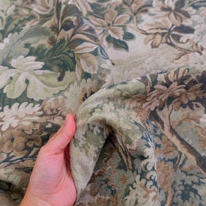 May include: A woven fabric featuring a dense, intricate botanical pattern in shades of sage green, olive, beige, and cream. The textile displays a repeating design of large, stylized leaves and floral elements with a textured, tapestry-like finish.