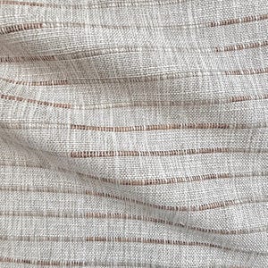Puede incluir: Primer plano de una tela texturizada con un patrón tejido. La tela es principalmente de color beige claro, con rayas horizontales de un tono marrón más oscuro. El tejido crea una textura sutil, similar a una cuadrícula.