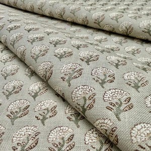 Puede incluir: Primer plano de una tela con un patrón floral repetitivo. Las flores son blancas con detalles marrones y tallos verdes, sobre un fondo verde claro. La tela está doblada, mostrando textura y profundidad.