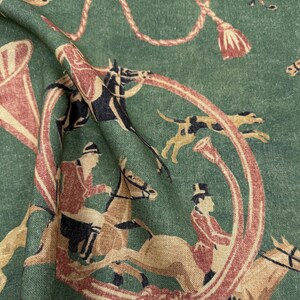 May include: Green fabric with a repeating equestrian design. The pattern features riders on horseback, hounds, and hunting horns in shades of brown, red, and cream. Decorative rope and tassel elements complete the design.