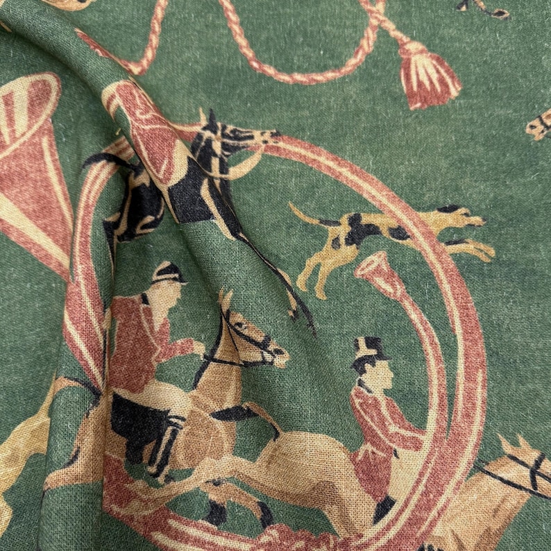 May include: Green fabric with a repeating equestrian design. The pattern features riders on horseback, hounds, and hunting horns in shades of brown, red, and cream. Decorative rope and tassel elements complete the design.