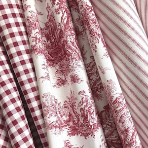 May include: Close-up of several fabric patterns. The fabrics include a red and white gingham check, a white fabric with a red toile de Jouy design, and a white fabric with red vertical stripes. The fabrics are folded and layered.