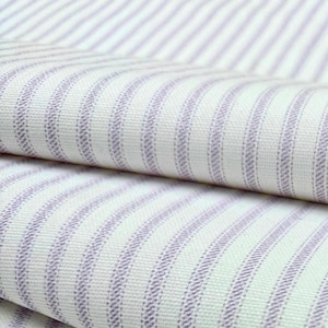 a close-up view of a fabric with a striped pattern in shades of white and purple. The fabric appears to be folded or rolled, with the edges of the fabric visible.