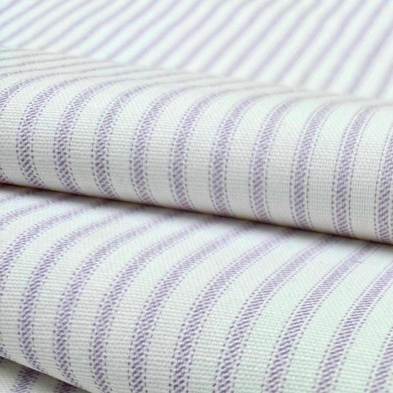 a close-up view of a fabric with a striped pattern in shades of white and purple. The fabric appears to be folded or rolled, with the edges of the fabric visible.