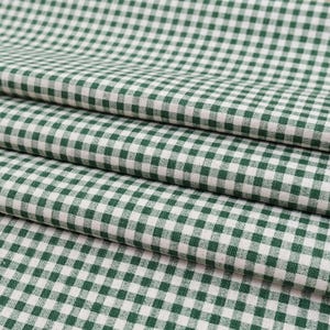 May include: A folded textile fabric featuring a classic gingham pattern with a repeating grid of dark forest green and off-white squares. The material displays a visible woven texture with consistent, uniform checks across the entire surface.