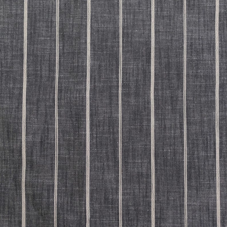 May include: Close-up of a fabric with a dark gray background and vertical white stripes. The fabric has a textured appearance, with the stripes evenly spaced across the surface. The stripes are thin and create a simple, classic pattern.