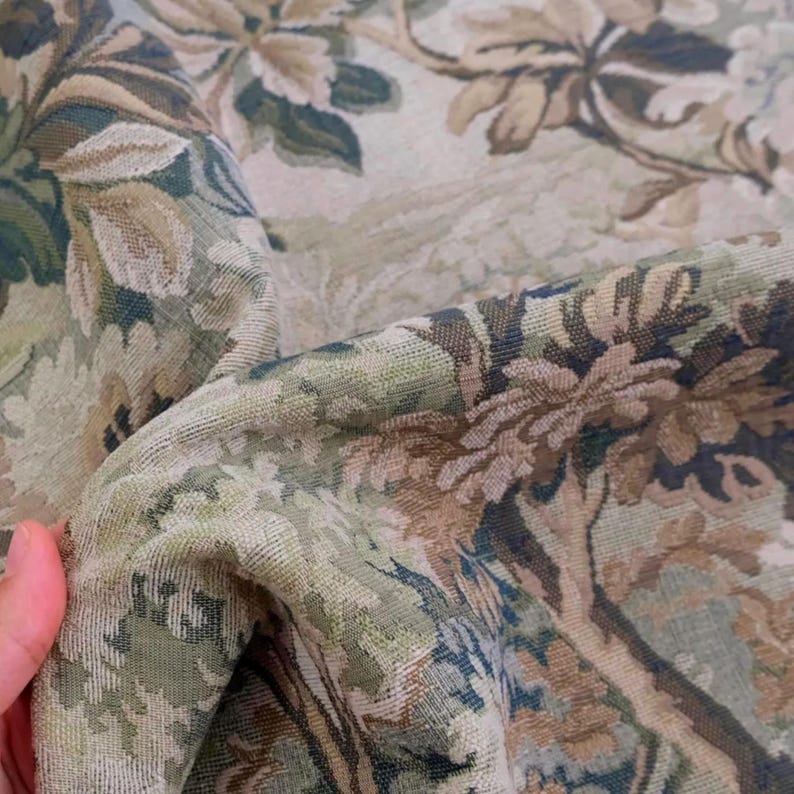 May include: A woven fabric featuring a detailed botanical pattern in shades of sage green, muted brown, and cream. The textile displays a dense, textured weave with intricate floral and leafy motifs that create a layered, multi-dimensional appearance.