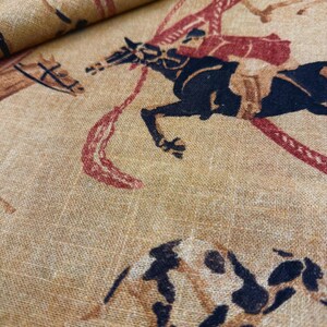 May include: Tan fabric with a repeating pattern of horses and riders in black, brown, and red. The horses are in motion, and the riders are depicted in a stylized manner. The fabric has a textured appearance, suggesting a linen or similar material.
