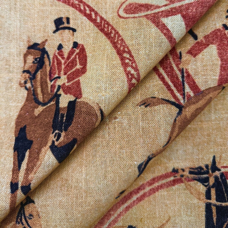 May include: Tan fabric with a repeating pattern of equestrian figures in red and brown. The design features riders on horseback, wearing riding attire, and a decorative circular border. The fabric has a textured appearance.