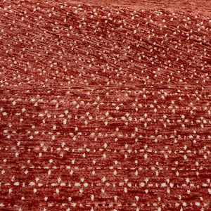 May include: A textured fabric featuring a deep terracotta red base color with a repeating pattern of small, white, four-pointed star or diamond shapes arranged in horizontal rows across the surface of the material.
