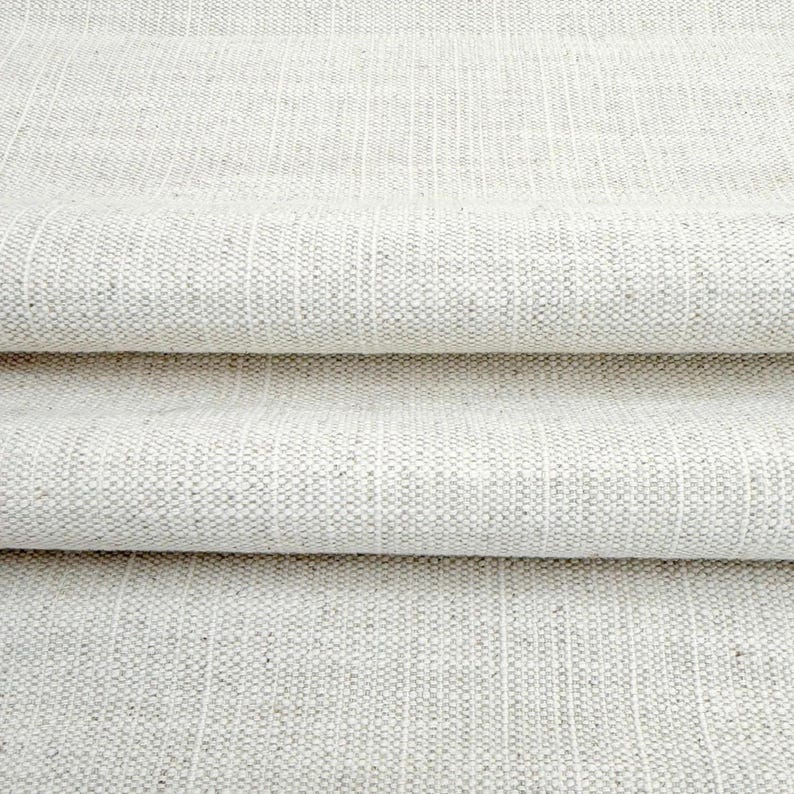 May include: A folded piece of off-white fabric with a visible woven texture. The material features a repeating pattern of vertical stripes created by subtle variations in the weave, resulting in a light beige and cream color palette throughout.