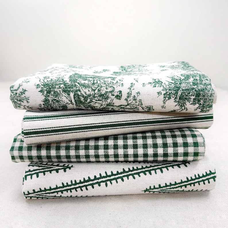 May include: A stack of four folded fabric napkins in white and forest green. The top napkin features a detailed pastoral toile print, the second has thin vertical stripes, the third displays a classic gingham check, and the bottom has a fern pattern.