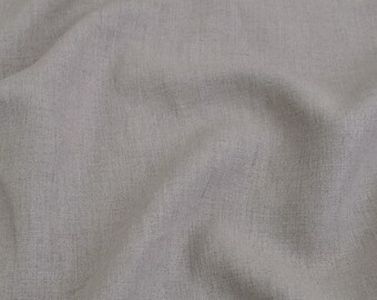 May include: A piece of light gray fabric with a visible woven texture and subtle variations in tone. The material is draped in soft, flowing folds, highlighting the natural weave and the matte finish of the textile surface throughout.