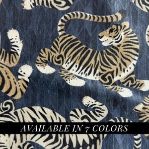 May include: A fabric featuring a repeating pattern of tigers in tan, black, and white against a dark blue background with a subtle diamond texture. The text "AVAILABLE IN 7 COLORS" is printed in white across the center of the image.