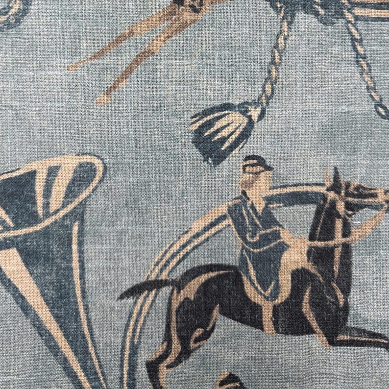 Puede incluir: Primer plano de una tela con un dise&ntilde;o ecuestre repetido. El patr&oacute;n presenta jinetes a caballo, borlas decorativas y formas de cuerno estilizadas en tonos azul marino, beige y marr&oacute;n sobre un fondo azul claro.