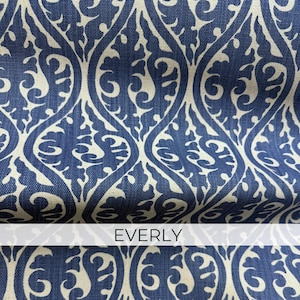 a close-up view of a fabric with a repeating pattern of blue and white swirls and curves. The fabric appears to be a type of upholstery or textile, with the word "EVERLY" written in white text on the fabric.