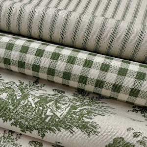 May include: Close-up of several rolls of fabric with different patterns. The top roll has vertical green stripes on a cream background. The middle roll features a green and white checkered pattern. The bottom roll displays a green toile design on a cream background.