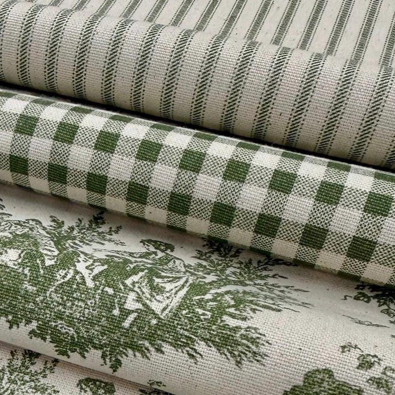 May include: Close-up of several rolls of fabric with different patterns. The top roll has vertical green stripes on a cream background. The middle roll features a green and white checkered pattern. The bottom roll displays a green toile design on a cream background.