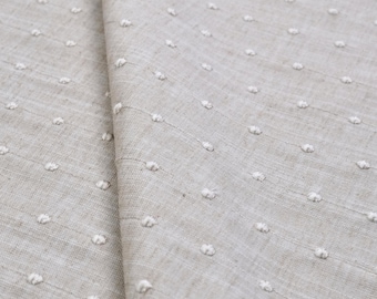 May include: A light beige fabric featuring a repeating pattern of small, raised white dots arranged in vertical lines. The textile has a visible woven texture with a consistent grid of embroidered tufted spots across the entire surface.
