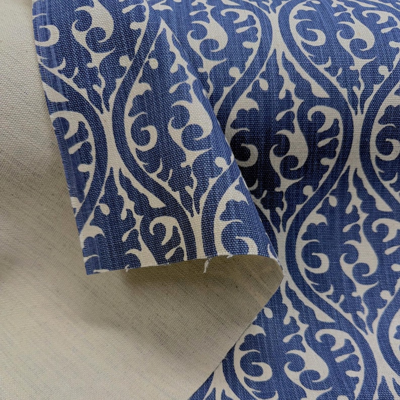 a close-up view of a fabric with a blue and white floral pattern. The fabric appears to be a piece of cloth or textile, with a repeating pattern of swirls and curves. The fabric is folded over itself, revealing the intricate design underneath. The fabric is predominantly blue, with white accents that add contrast to the overall pattern. The image does not contain any text or other objects, and the focus is solely on the fabric and its design.
