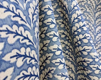 May include: A woven fabric featuring a repeating pattern of white oak leaves set against a medium blue background. The material displays a visible textile weave and is draped to create soft folds that highlight the botanical print design.