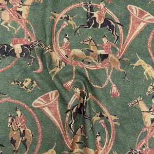 May include: Green fabric with a repeating pattern of equestrian figures, hounds, and hunting horns in shades of red, brown, and black. The design features riders on horseback, dogs, and decorative horn shapes.