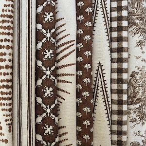 Könnte beinhalten: Eine Auswahl an braunen und cremefarbenen Stoffmustern. Die Muster umfassen Punkte, Streifen, Blumenmuster, geometrische Muster und Toile-de-Jouy-Designs. Die Stoffe sind vertikal angeordnet und zeigen eine Vielzahl von Texturen und Stilen, die sich für Heimdekoration oder Bastelprojekte eignen.