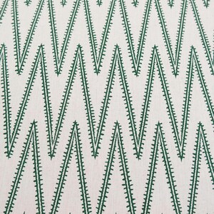 May include: A textile fabric featuring a repeating geometric chevron pattern in dark green thread embroidered onto a light cream-colored background. The zigzag lines are composed of small, dense stitches that create a textured, linear appearance.