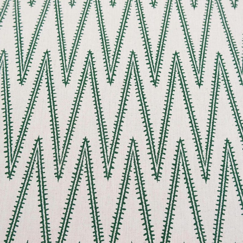 May include: A textile fabric featuring a repeating geometric chevron pattern in dark green thread embroidered onto a light cream-colored background. The zigzag lines are composed of small, dense stitches that create a textured, linear appearance.
