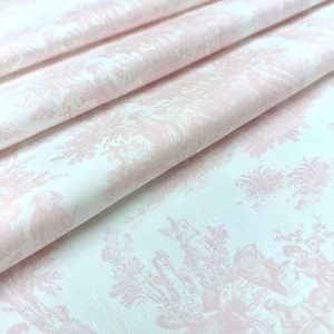 May include: A folded piece of fabric featuring a light pink toile de jouy pattern on a white background. The textile displays intricate, repeating pastoral scenes with figures and foliage printed in a soft, monochromatic pink ink.