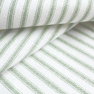 a close-up view of a fabric with a striped pattern in shades of green and white. The fabric appears to be folded or rolled, creating a visually interesting and textured surface.