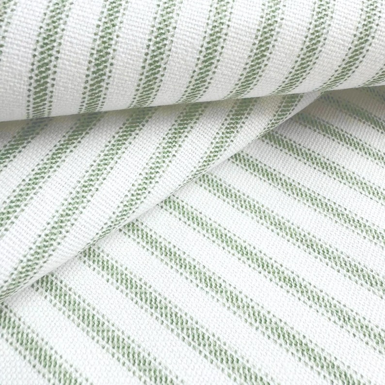 a close-up view of a fabric with a striped pattern in shades of green and white. The fabric appears to be folded or rolled, creating a visually interesting and textured surface.