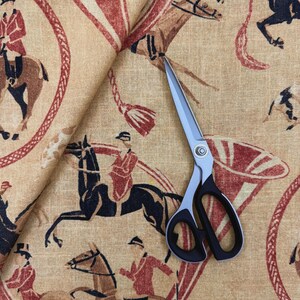 May include: Tan fabric with a repeating equestrian design in red, brown, and black. The pattern features riders on horseback, decorative elements, and a pair of open scissors.