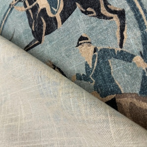 Puede incluir: Primer plano de una tela con un dise&ntilde;o ecuestre vintage. La tela presenta un fondo azul claro con un patr&oacute;n repetido de un caballo y un jinete en tonos azul marino, beige y marr&oacute;n. La tela est&aacute; doblada, revelando un reverso beige claro liso.