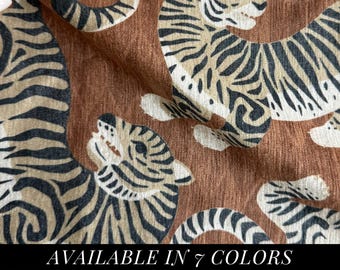 May include: A textured fabric featuring a repeating pattern of tigers in beige and black against a solid brown background. The tigers are depicted in various poses with visible stripes and facial details. The text AVAILABLE IN 7 COLORS is printed.