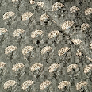 May include: A woven fabric featuring a repeating pattern of small, stylized beige flowers with dark stems and light blue leaves set against a textured, dark olive green background. The material has a visible grid-like weave and a folded corner.