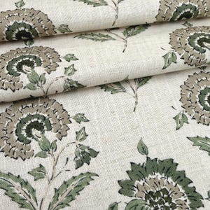 May include: Close-up of a cream-colored fabric with a repeating floral pattern. The design features large, stylized flowers in shades of green and taupe, with detailed leaves and stems. The fabric has a textured appearance.