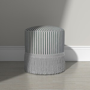 May include: A cylindrical ottoman featuring a vertical striped pattern in dark green and off-white. The base of the ottoman is adorned with a thick, textured light gray fringe trim that encircles the entire bottom edge of the piece.