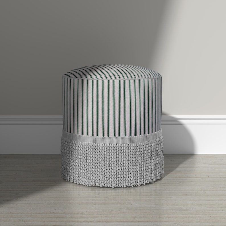 May include: A cylindrical ottoman featuring a vertical striped pattern in dark green and off-white. The base of the ottoman is adorned with a thick, textured light gray fringe trim that encircles the entire bottom edge of the piece.