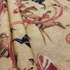 May include: Tan fabric with a repeating equestrian design. The fabric features illustrations of riders on horseback, in shades of brown, red, and black. The fabric is folded, showing the texture and drape of the material.