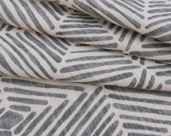 May include: A piece of fabric featuring a repeating geometric pattern of dark gray lines on an off-white background. The design consists of hexagonal shapes formed by parallel lines, with the fabric folded to show depth and texture.