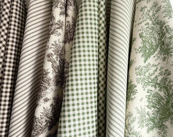 Pode incluir: Uma coleção de seis rolos de tecido com vários padrões, incluindo xadrez vichy castanho e branco, riscas castanhas e brancas, toile castanho, xadrez vichy verde e branco, riscas verdes e brancas e toile verde com cenas pastorais detalhadas.