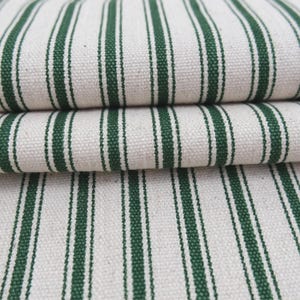May include: A folded piece of heavy-duty fabric featuring a repeating pattern of vertical dark forest green stripes against a natural off-white, cream-colored background. The textile displays a visible, coarse woven texture with a sturdy appearance.