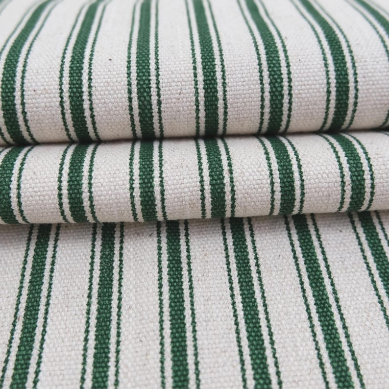 May include: A folded piece of heavy-duty fabric featuring a repeating pattern of vertical dark forest green stripes against a natural off-white, cream-colored background. The textile displays a visible, coarse woven texture with a sturdy appearance.